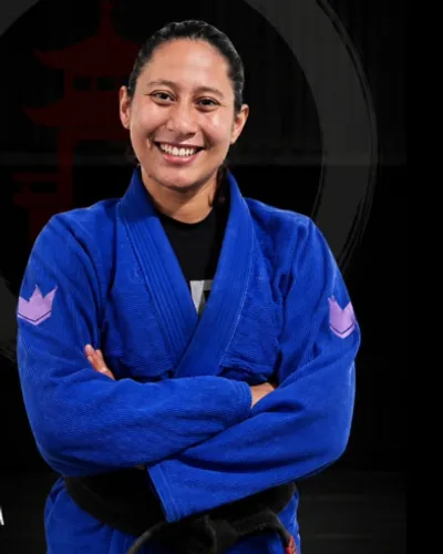 Professora Karen sorrindo, de braços cruzados, com kimono azul e faixa preta